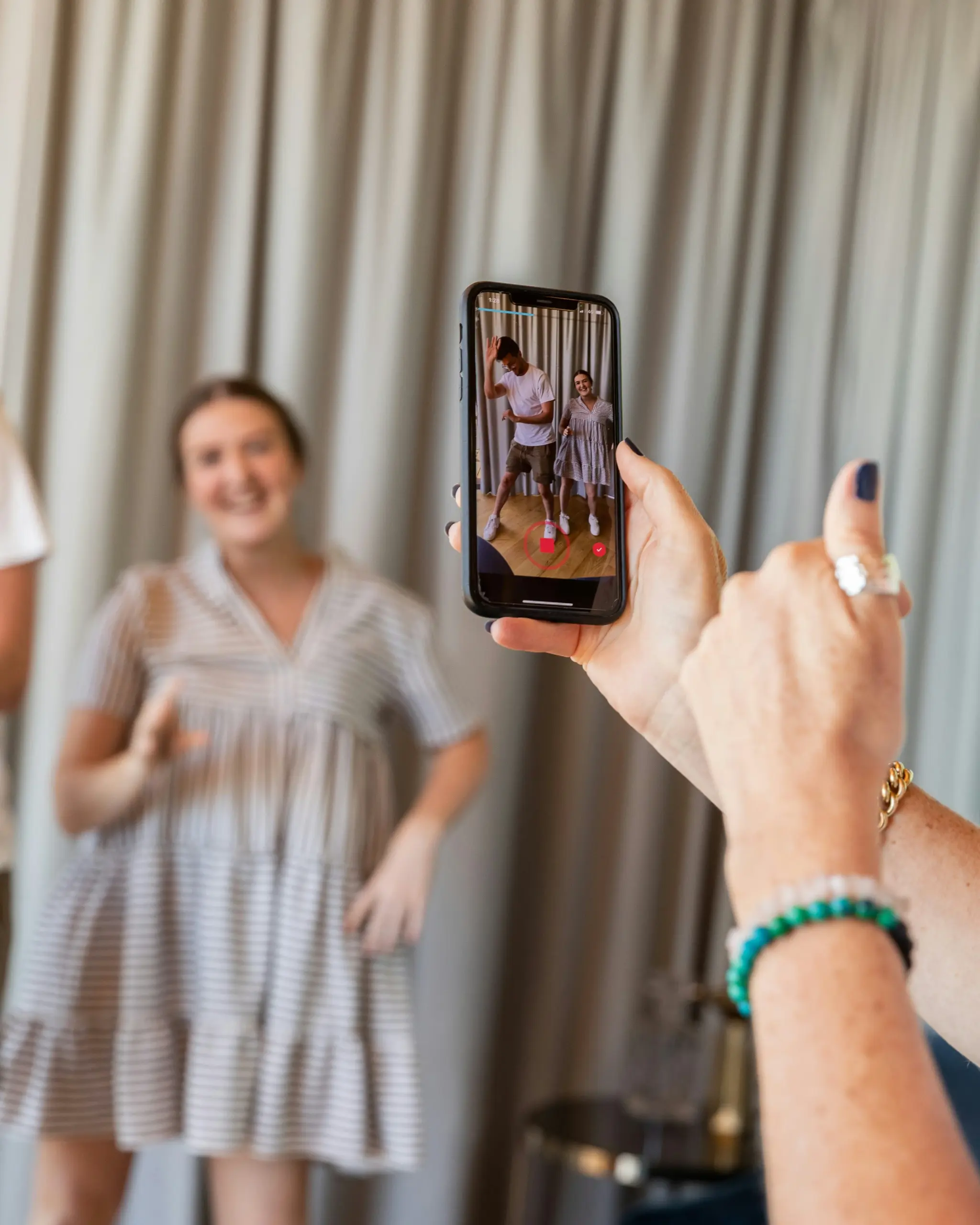 A photo of a person filming a TikTok dance video on their smartphone featuring two people smiling in front of a curtain.