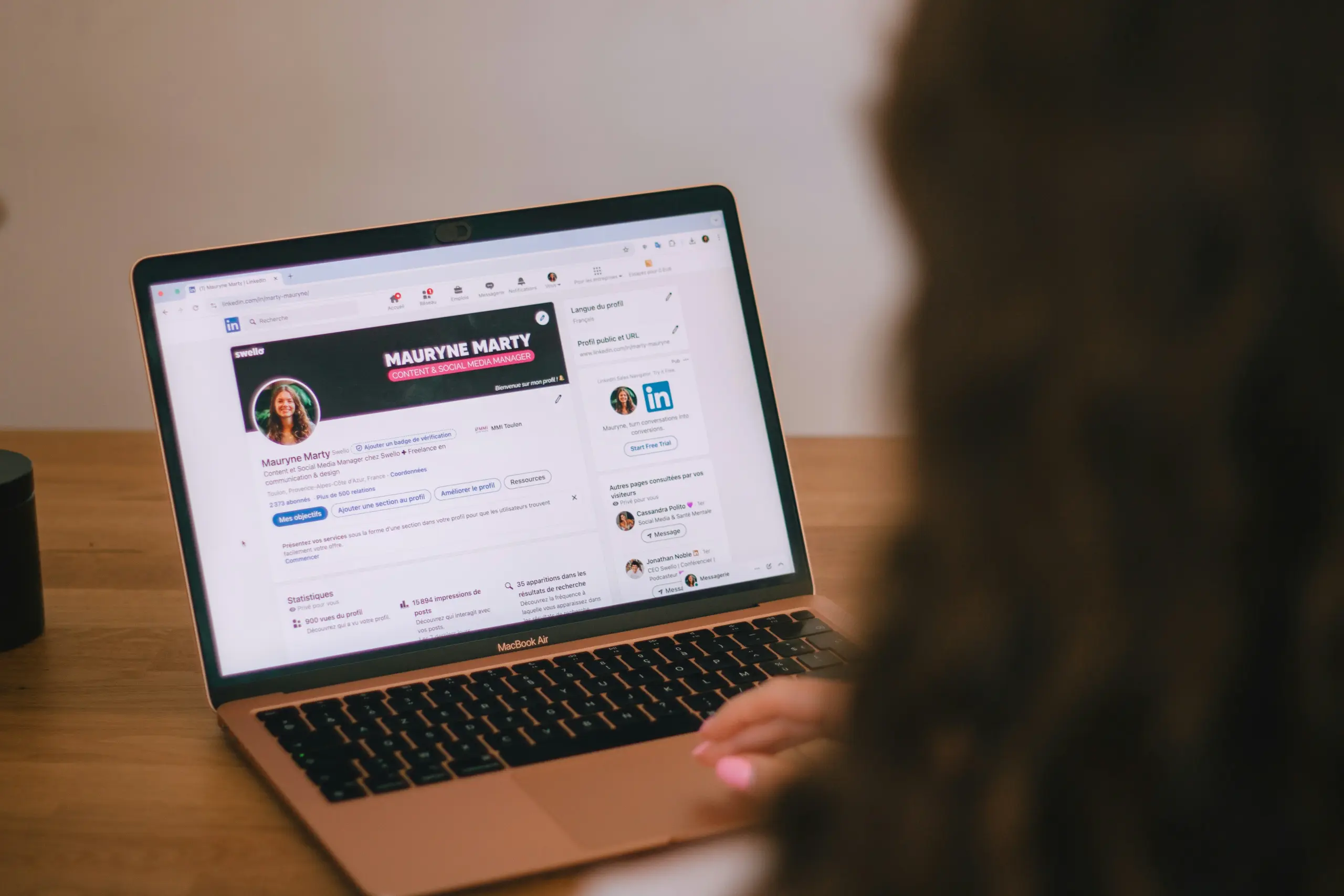 Photo of a woman browsing a LinkedIn profile page on her rose gold MacBook Air at a wood table